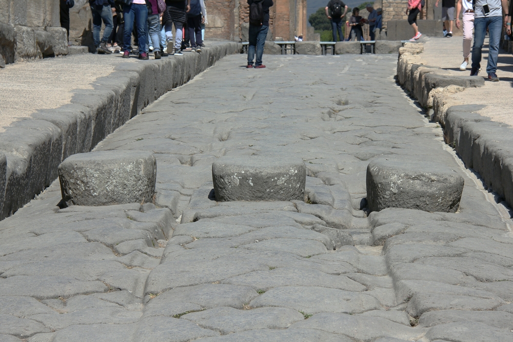 On the Via Stabiana, one of the main Roman roads through the city, showing the stepping-stones used to cross the often filthy road, and the grooves
        where wagon wheels had ground away the basalt paving blocks.