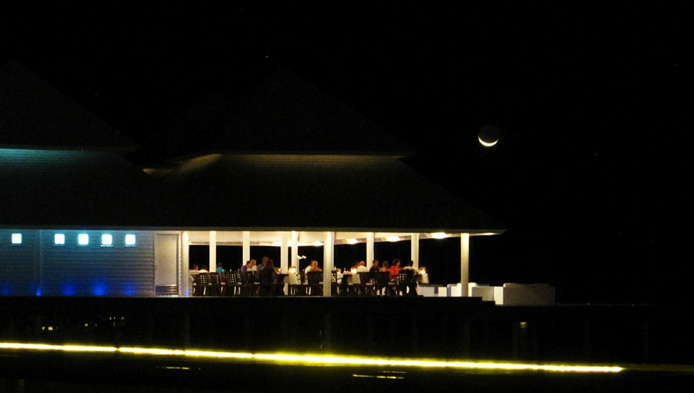 The new moon hangs over the Water Villa restaurant at night.