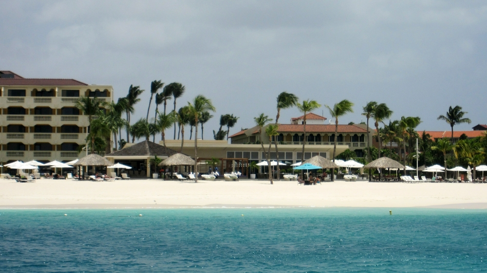 Bucuti Hotel and Tara Suites from the dive boat. The Tara Suites building is at the left, and the Bucuti building at middle right. 
						The low white building in front of Bucuti is the main restaurant, Elements. The Sandbar is to the left of Elements. The blue sun 
						umbrella is the smoking sun umbrella. Smoking was prohibited at all other areas on the beach.