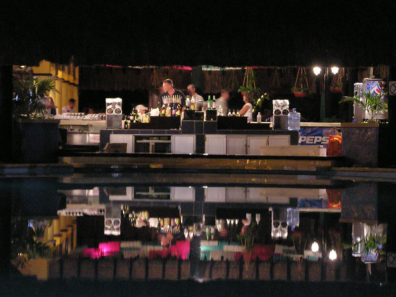 Customers waiting at the pool bar, reflected in the pool late at night. (97k)