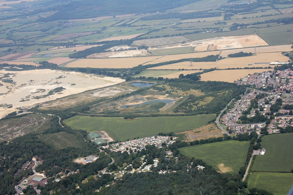 The village of Crossways, Dorset is at the right. RAF Warmwell used to be on the area to the left of the village. Millions of tons of 
					gravel have been extracted from the site. The two large green buildings just below and to the left of centre are all that remains of 
					RAF Warmwell - two aircraft hangars, now used as storage barns by a local farmer.