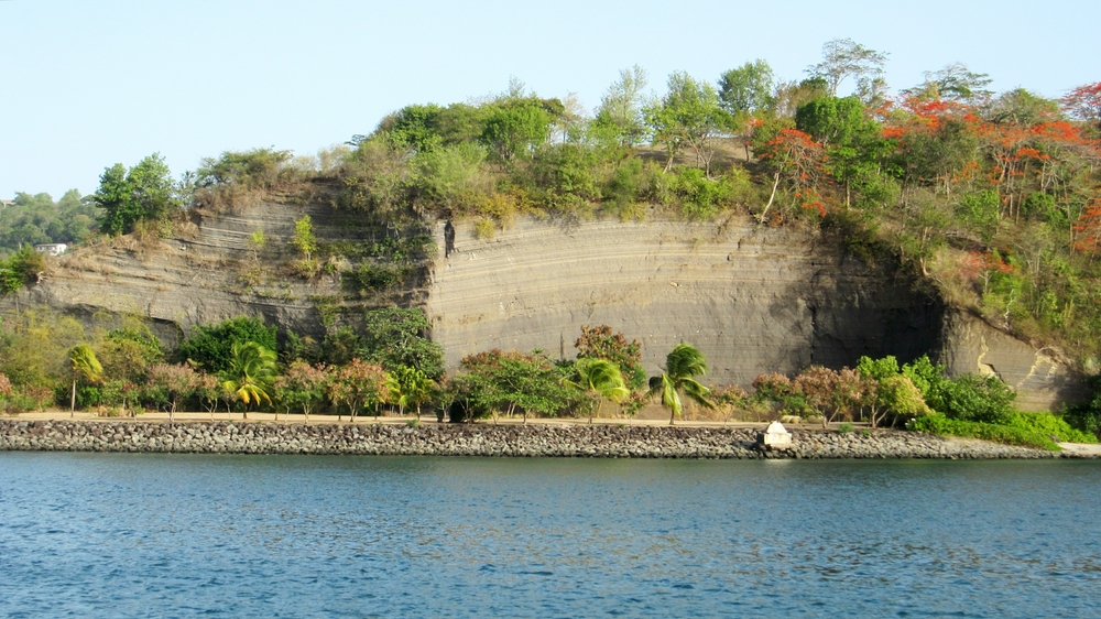 Layers of ash beside the Carenage reveal Grenada's volcanic origins. The flowers of the Flamboyant trees at the top right are a vivid orange.