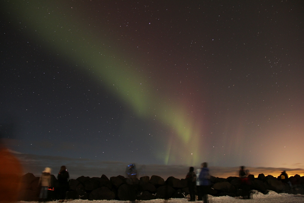 My first sight of the Northern Lights, off to the east, with a red and green curtain. At this point, it's almost invisible 
						to the naked eye. The glare lighting the clouds in the bottom-right of the picture is coming from Keflavik airport a few miles 
						away.  Canon EOS 550D, Canon 18-200mm lens, at wide angle, f3.5, ISO 800, exposure time 30 seconds. 