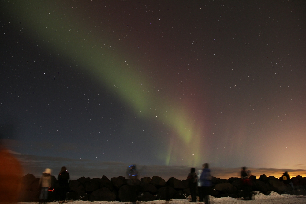 My first sight of the Northern Lights, off to the east, with a red and green curtain. At this point, it's almost invisible 
						to the naked eye. The glare lighting the clouds in the bottom-right of the picture is coming from Keflavik airport a few miles 
						away.  Canon EOS 550D, Canon 18-200mm lens, at wide angle, f3.5, ISO 800, exposure time 30 seconds. 