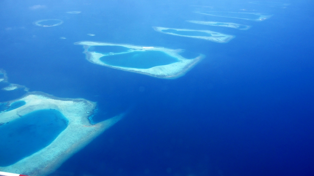 The eastern edge of Ari Atoll, as seen from the seaplane at about 2000 feet. Deep water on the right, shallower on the left. Some of the 
					numerous reefs marking the edge of the atoll form a straight line. There's a small yellowy sandbank just sticking its head above water 
					just above the middle of the photo. Everything else is seen through a couple of metres of transparent ocean.