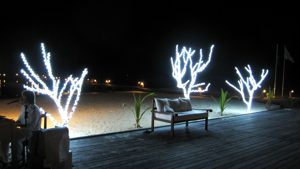 More festive lights in front of Reception, while the singer plays piano to entertain a party having a formal dinner on the beach. 