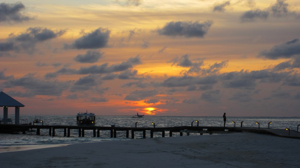 Sunset over the jetty at Thudufushi. A Twin Otter seaplane is tied up to the pontoon in the lagoon, ready for an early flight back 
					to Male in the morning. The crew stay on the island overnight - a tough job, but somebody's got to do it.
