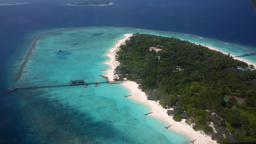 Meedhupparu island in Raa Atoll at last. The long south jetty is to the left, with the dive centre's kit store and compressor room in the 
				building half-way along. Photo taken from the left side of the aircraft. We'll shortly bank round to the left and circle the island before 
				landing at the left of the photo, and then enter the lagoon to tie up alongside one of the two floating pontoons attached to this side of the jetty.