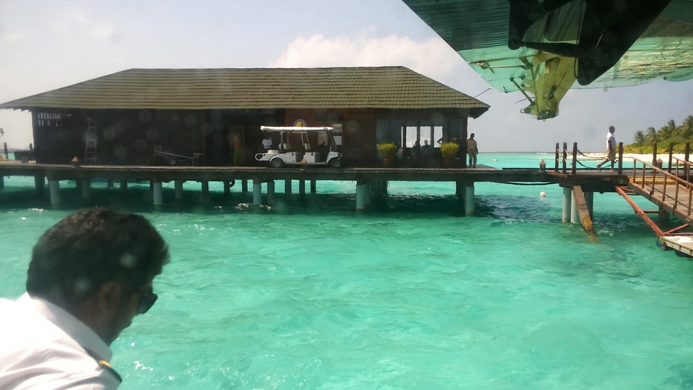 Preparing to tie up at one of the pontoons. One of the seaplane crew has jumped down onto the float to get the mooring line ready. The dive centre's building, 
					with a golf buggy parked in front of it ready to take passengers to Reception.	The seaplane's window is freshly splashed with salty water from the landing.