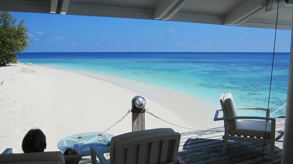 Relaxing on the Main Bar's deck with a glass of bubbly. What a view - the blinding-white coral sand, and the blues of the house reef, the deeper
        water beyond, and the sky.