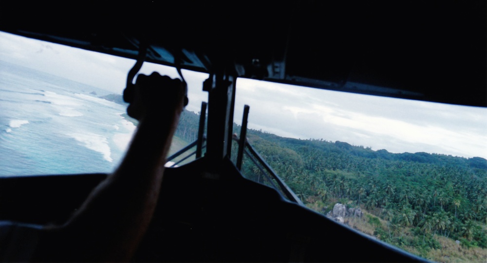 Our Twin Otter coming in to land on the grass airstrip at Frigate Island.  The airstrip is mostly hidden
            behind the pilot's wrist, but this shows the narrow gap between the palm trees and the beach.